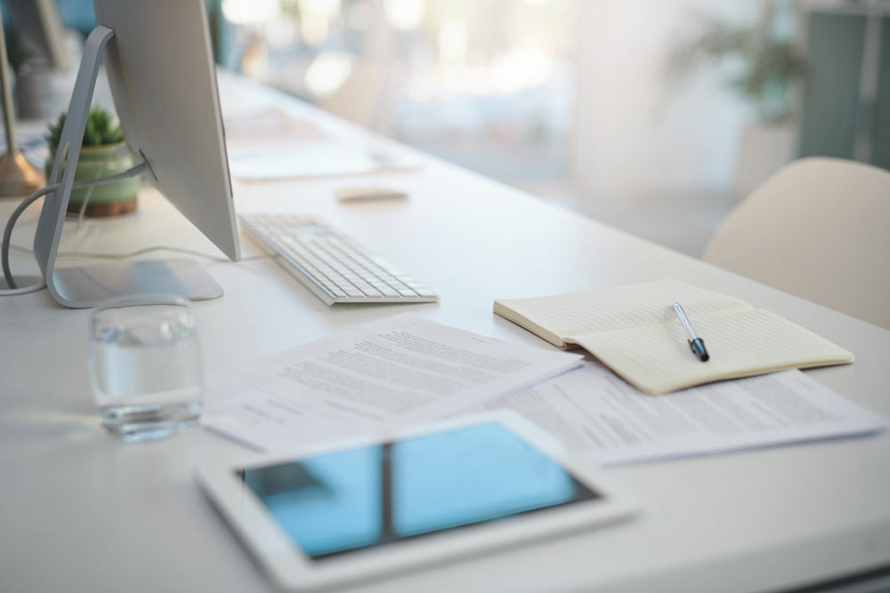 Ett vitt skrivbord med en dator och en anteckningsbok